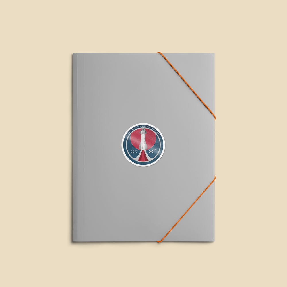 A gray notebook or journal with an orange elastic closure band and a circular red, white, and blue peace sticker in the center, shown on a solid beige background.