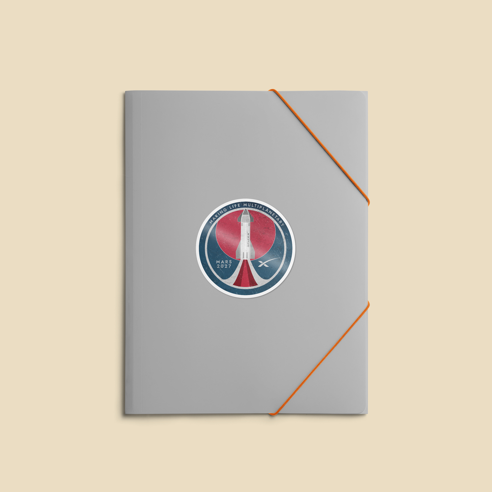 A gray notebook or journal with a circular space-themed sticker on the front, secured with an orange elastic band, set against a solid beige background.