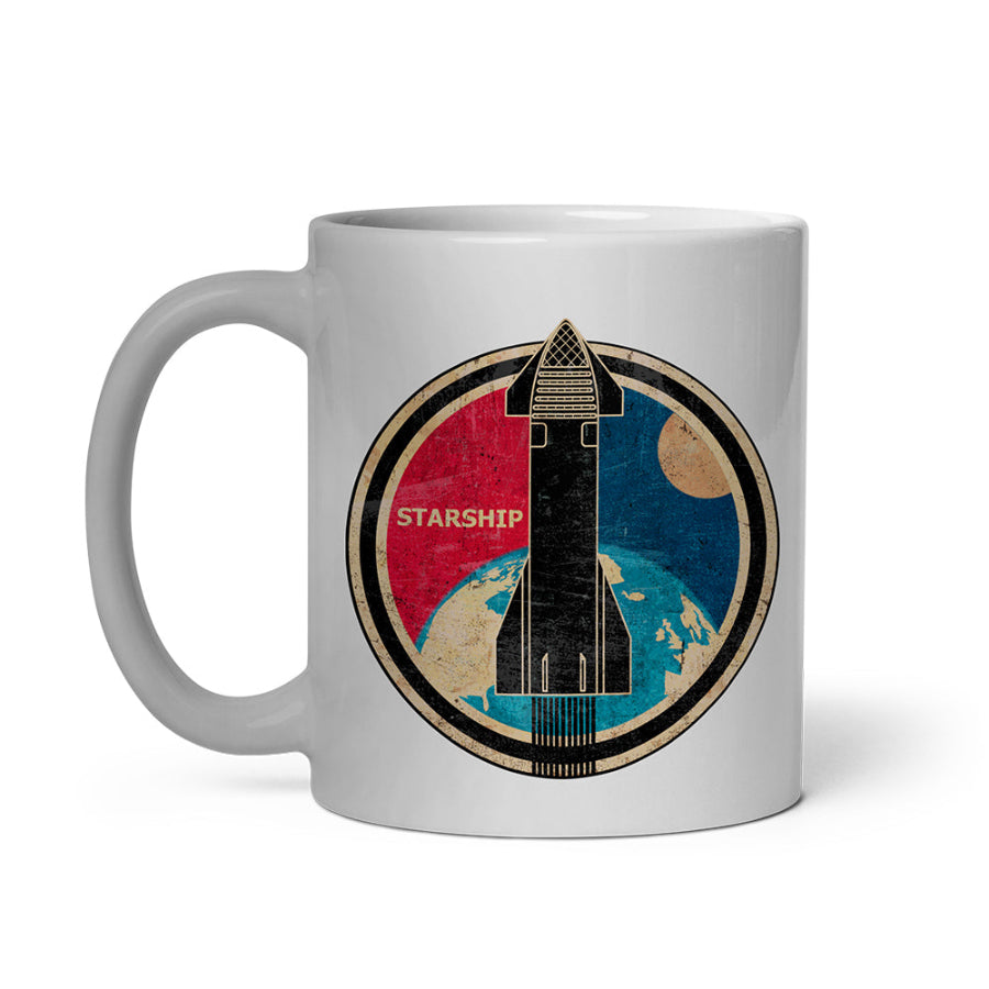 A white ceramic mug featuring a circular graphic of a black Starship rocket launching over a blue and beige globe, with a red sun and dark blue sky in the background.